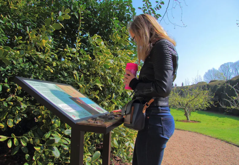 Woman reading sign in garden.
